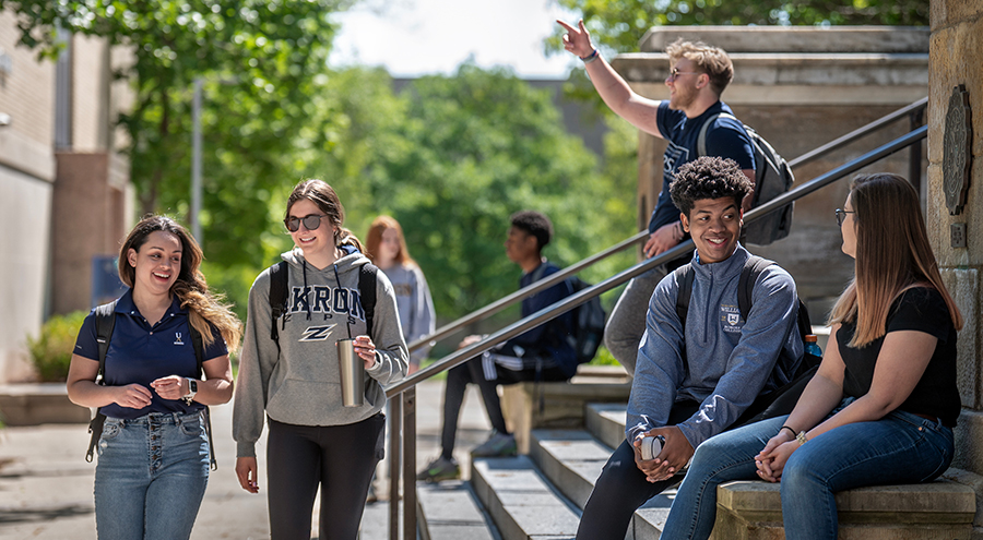 Happy MŮ students walking out of and in front of Buchtel Hall on The University of Akron campus.